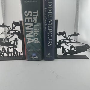 May include: Black metal bookends with a DeLorean car design. The bookends have the words "BACK IN TIME" cut out at the base. Two books are held between the bookends. One book is titled "The Life of Senna".