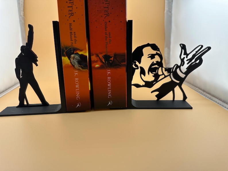 K&ouml;nnte beinhalten: Schwarze Metall-Buchst&uuml;tzen mit Silhouetten eines S&auml;ngers in ikonischen Posen. Eine Buchst&uuml;tze zeigt eine Figur mit erhobenem Arm, die andere einen S&auml;nger mit Mikrofon. Die Buchst&uuml;tzen sind zum Halten von B&uuml;chern konzipiert.