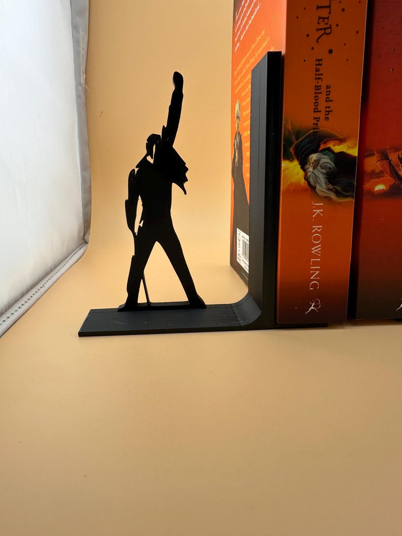 K&ouml;nnte beinhalten: Schwarzer Metall-Buchst&uuml;tze mit einer Silhouette einer Person mit erhobenem Arm. Die Buchst&uuml;tze befindet sich neben einem Stapel B&uuml;cher mit orangefarbenen Einb&auml;nden. Die Buchst&uuml;tze dient dazu, B&uuml;cher aufrecht zu halten.