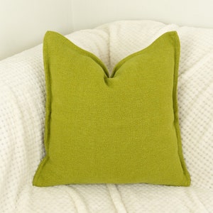 May include: A bright green square cushion on a white textured surface.