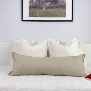Peut inclure: Un coussin lombaire en lin beige posé sur un lit blanc avec des coussins en lin blanc derrière.