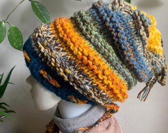 May include: A handmade, colorful knit beanie in shades of blue, orange, green, and yellow. The hat has a textured, chunky knit design and a long, slouchy fit. The beanie is a stylish accessory for cold weather.