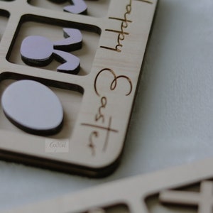 May include: Wooden puzzle with a light pink bunny and egg shapes. The puzzle is labeled "Happy Easter".