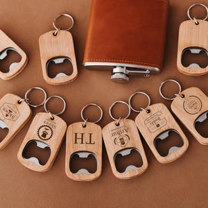 Peut inclure: Dix porte-clés ouvre-bouteille en bois avec différents motifs gravés. Chaque porte-clés est doté d'un ouvre-bouteille en argent et d'un anneau pour attacher les clés. Les porte-clés sont sur une surface brune.
