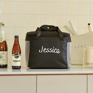 Pu&ograve; includere: Borsa termica nera con chiusura a zip e bordatura grigia. La borsa ha il nome "Jessica" ricamato in bianco sul davanti.