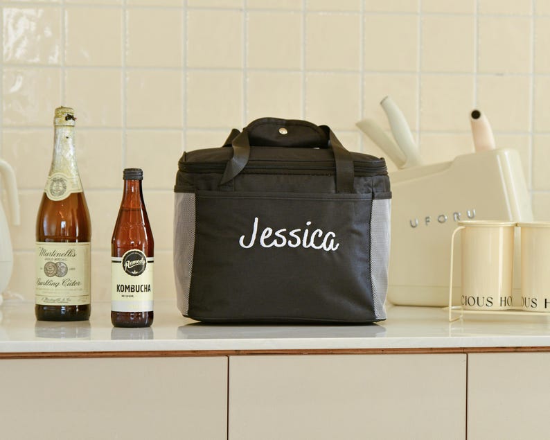 Pu&ograve; includere: Borsa termica nera con chiusura a zip e bordatura grigia. La borsa ha il nome "Jessica" ricamato in bianco sul davanti.