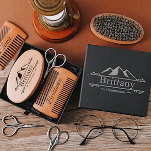 Könnte beinhalten: Eine schwarze Geschenkbox mit einem Bergmotiv und dem Namen "Brittany" eingraviert. Die Box enthält einen Holzkamm, eine Holzbürste und eine Schere. Der Kamm und die Bürste sind ebenfalls mit dem Namen "Brittany" graviert.