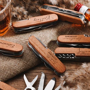 Peut inclure: Un ensemble de six couteaux de poche personnalis&eacute;s avec des manches en bois. Chaque couteau porte un nom grav&eacute; diff&eacute;rent sur le manche, notamment "Elliott", "Jessica", "Bride", "Angela", "Groom" et "Brittney".