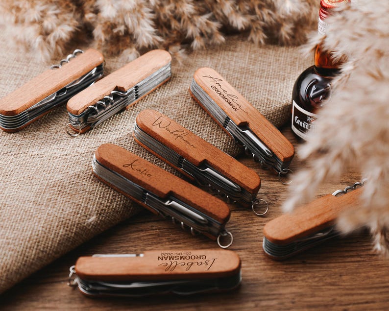 Peut inclure: Ensemble de couteaux de poche en bois personnalis&eacute;s avec des noms grav&eacute;s. Chaque couteau a un manche en bois brun et une lame argent&eacute;e. Les couteaux sont dispos&eacute;s sur une surface brune.