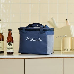 Pu&ograve; includere: Una borsa termica per il pranzo blu e grigia con chiusura a zip e una tasca laterale in rete. La borsa ha la parola "Mahault" ricamata in bianco sul davanti.