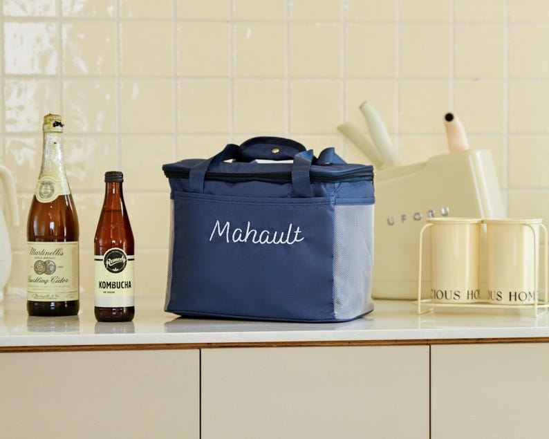 Pu&ograve; includere: Una borsa termica per il pranzo blu e grigia con chiusura a zip e una tasca laterale in rete. La borsa ha la parola "Mahault" ricamata in bianco sul davanti.