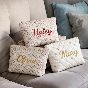 May include: Three personalized cosmetic bags. Two are patterned with a floral design and the names "Haley" and "Olivia" embroidered in red and gold. The third is quilted with the name "Mary" embroidered in gold.