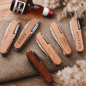 May include: Five wooden pocket knives with personalized names, including "Josef", "William", "Mary Jo", and "Best Man,  Groomsman". The knives have a brown wooden handle and silver metal blades.