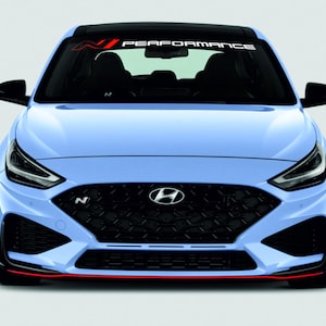 以下が含まれることがあります： フロントビューのライトブルーのヒュンダイ車。黒いグリルと赤いアクセントが特徴です。フロントガラスの上部には「PERFORMANCE」の文字があります。ヒュンダイのロゴが前面に表示されています。
