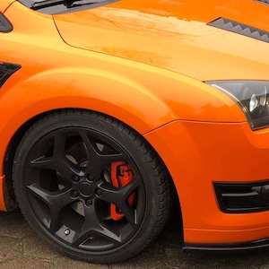 May include: A bright orange Ford Focus ST with black aftermarket side vents and black wheels. The car has a black front bumper and black accents around the headlights.