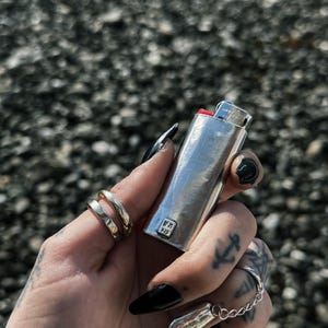 May include: A silver lighter with a red top and the text "WM 925" on the side. The lighter is being held by a hand with black nail polish.