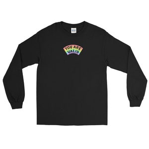 May include: Black long-sleeve shirt with the text "YOU ARE VALID" in a rainbow arc design. The shirt is made of a soft material and has long sleeves. The shirt is a crew neck.