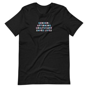 May include: Black t-shirt with the text "GENDER-AFFIRMING HEALTHCARE SAVES LIVES" in pastel colors. The text is stacked in four lines. The shirt is made of a soft material and has short sleeves and a crew neck.