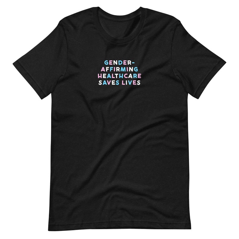 May include: Black t-shirt with the text "GENDER-AFFIRMING HEALTHCARE SAVES LIVES" in pastel colors. The text is stacked in four lines. The shirt is made of a soft material and has short sleeves and a crew neck.