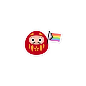 May include: A red and gold daruma doll with a smiling face and a black mustache, holding a rainbow pride flag.