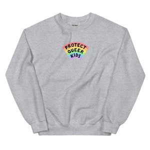 Puede incluir: Una sudadera gris jaspeada con un arcoíris y el texto "PROTECT QUEER KIDS" en negro.