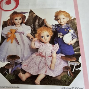 以下が含まれることがあります： 顔と髪が描かれた磁器製のドールが3体。左のドールはピンクのリボンが付いた白いドレスを着て、テディベアを持っています。真ん中のドールはピンクと白のドレスを着て、ピンクのリボンが付いています。右のドールは白鳥を持った青と白のドレスを着ています。ドールはキノコの形をした台座の上に座っています。ドールサイズ8インチ（20cm）。