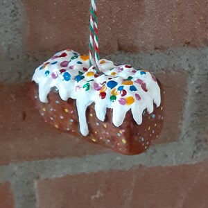 Peut inclure: Un g&acirc;teau glac&eacute; blanc avec des p&eacute;pites color&eacute;es suspendu &agrave; une ficelle rouge et verte. Le g&acirc;teau est d&eacute;cor&eacute; de gla&ccedil;age blanc et de p&eacute;pites color&eacute;es.