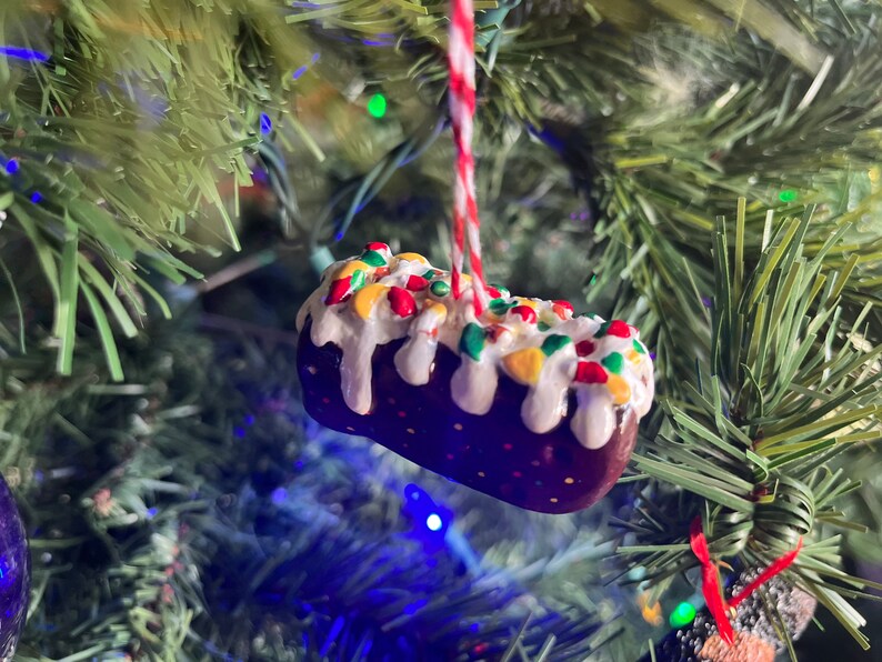 Peut inclure: Une d&eacute;coration de No&euml;l en forme de g&acirc;teau, de couleur marron et blanche, avec des vermicelles color&eacute;s et un gla&ccedil;age blanc.