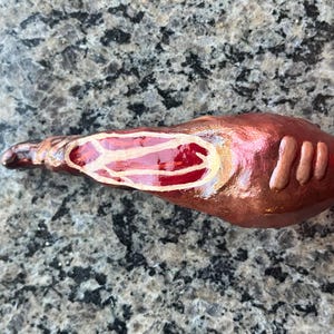 May include: A hand-painted ceramic sculpture of a red and gold fish with white details. The fish has a long, slender body and a slightly curved tail.