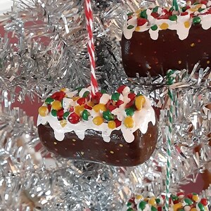 Peut inclure: Trois d&eacute;corations de No&euml;l en forme de g&acirc;teau au chocolat avec gla&ccedil;age blanc et p&eacute;pites color&eacute;es. Les d&eacute;corations sont suspendues &agrave; un sapin de No&euml;l en tinsel argent&eacute;.