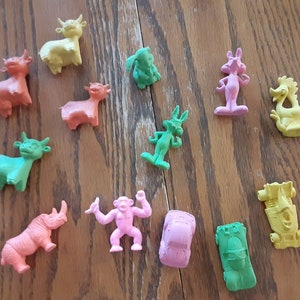 May include: A collection of 13 colorful plastic animal figurines, including a rhino, a monkey, a bull, a horse, a bird, and a rabbit. The figurines are all different colors, including green, pink, yellow, and orange.