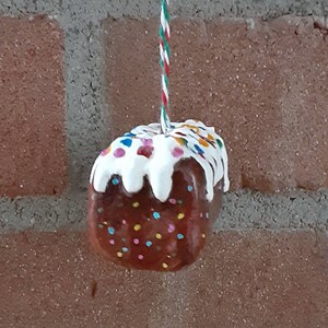 Peut inclure: Une d&eacute;coration de pain d'&eacute;pices marron et blanc avec des p&eacute;pites color&eacute;es suspendue &agrave; une ficelle rouge et blanche.
