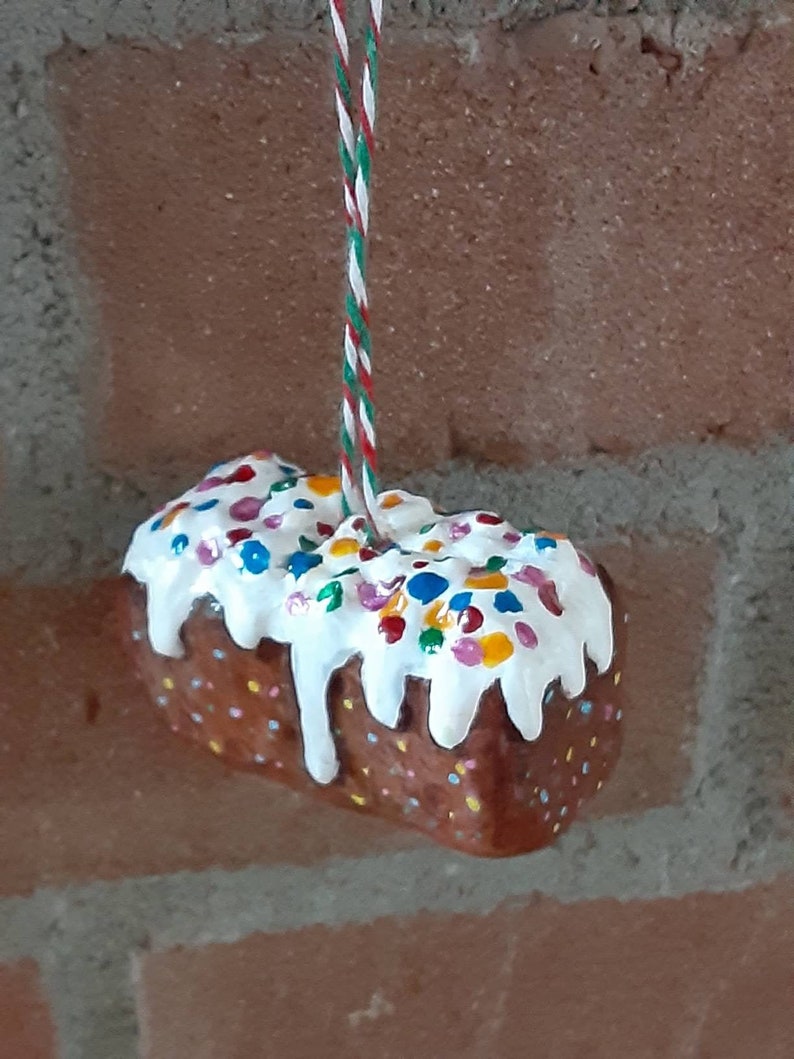 Peut inclure: Un g&acirc;teau glac&eacute; blanc avec des p&eacute;pites color&eacute;es suspendu &agrave; une ficelle rouge et verte. Le g&acirc;teau est d&eacute;cor&eacute; de gla&ccedil;age blanc et de p&eacute;pites color&eacute;es.