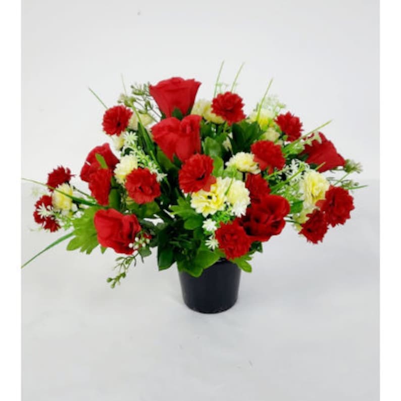May include: A red and white artificial flower arrangement in a black pot. The arrangement features red roses and carnations with white carnations.