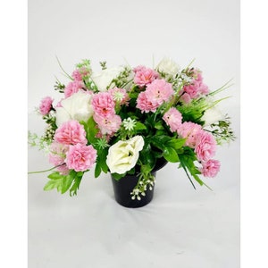 May include: A pink and white artificial flower arrangement in a black pot. The arrangement features pink carnations and white roses.