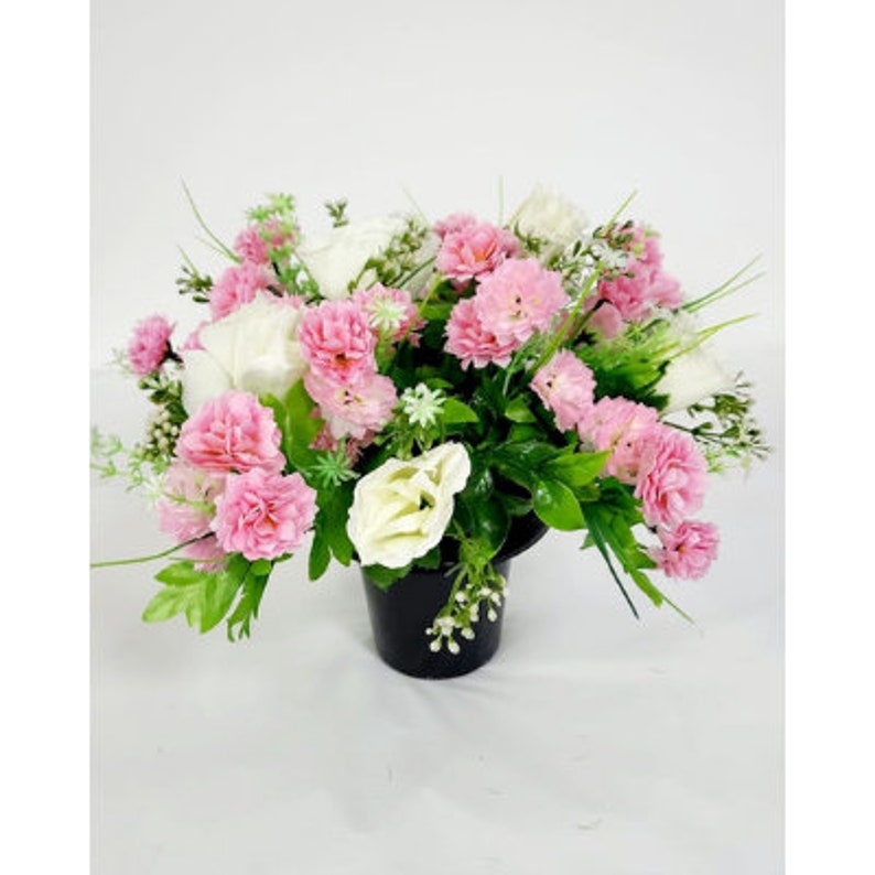May include: A pink and white artificial flower arrangement in a black pot. The arrangement features pink carnations and white roses.