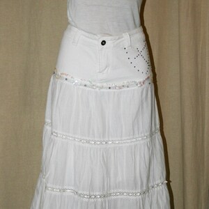May include: White tiered skirt with a white tank top. The skirt has a denim waistband with embellishments.