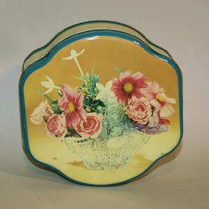 May include: A vintage tin box with a yellow background and a blue border. The box features a colourful floral arrangement of pink, white, and red flowers in a clear glass vase.
