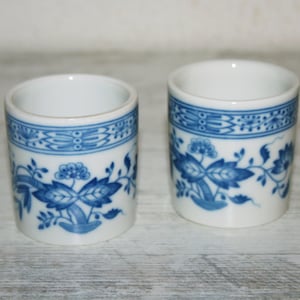 Può includere: Due porta uova in ceramica bianca con un motivo floreale blu. Le tazze hanno uno sfondo bianco con un motivo floreale blu e una fascia blu intorno alla parte superiore.