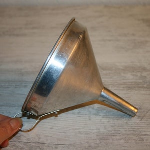 Puede incluir: Un embudo de acero inoxidable con boca ancha y boquilla estrecha. El embudo tiene un pequeño lazo de alambre para colgar. El artículo es de metal brillante y está diseñado para transferir líquidos o polvos.
