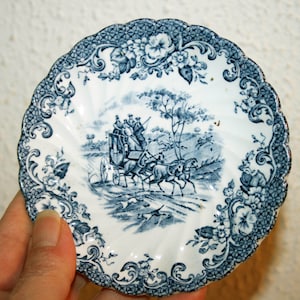 Könnte beinhalten: Eine blaue und weiße Porzellansaucers mit einem floralen Rand und einem zentralen Bild einer Kutsche, die von Pferden gezogen wird. Die Saucers hat einen gewellten Rand.