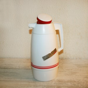 Può includere: Caraffa termica bianca con coperchio rosso e dettagli rossi. La caraffa ha un'etichetta che recita "Botella Interior de Acero Inoxidable. Mantiene mas de 8 horas.  Recargable."