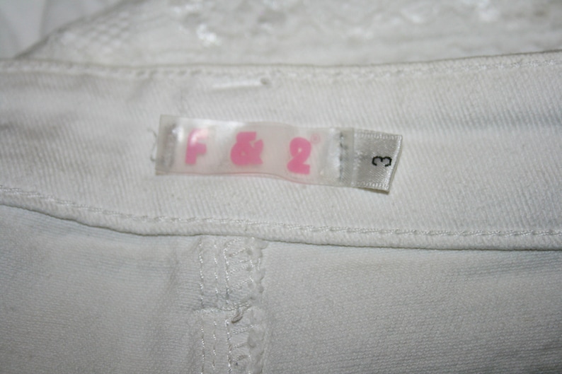 May include: White clothing label with pink lettering that reads "F&2" and a number "3" on a white background.