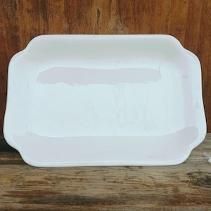 Può includere: Un piatto da portata rettangolare in ceramica bianca con bordi leggermente arrotondati. Il piatto ha una finitura liscia e lucida.