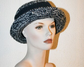 May include: A black and white crocheted hat with a wide brim. The hat is on a white mannequin head.