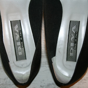 K&ouml;nnte beinhalten: Ein Paar schwarze Schuhe mit silbernem Futter und dem Text "DIVA MADE IN ITALY" auf der Innenseite.
