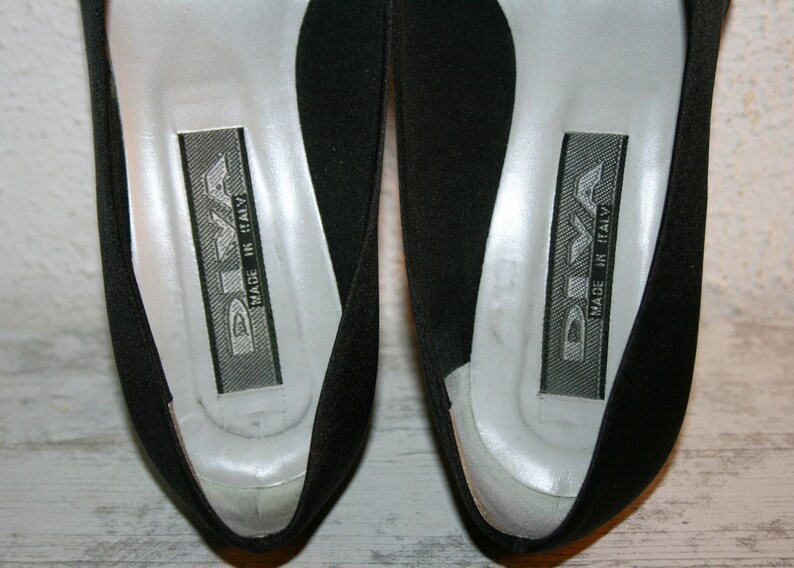 K&ouml;nnte beinhalten: Ein Paar schwarze Schuhe mit silbernem Futter und dem Text "DIVA MADE IN ITALY" auf der Innenseite.