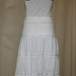 May include: White sleeveless top with a racerback design paired with a white tiered skirt with lace trim.