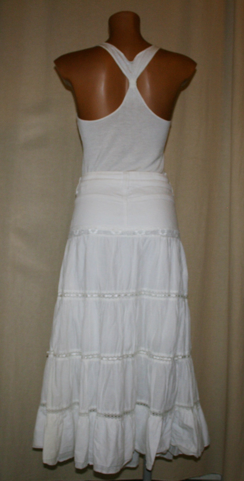 May include: White sleeveless top with a racerback design paired with a white tiered skirt with lace trim.