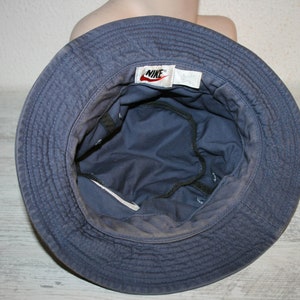 May include: A blue bucket hat with a Nike logo on the front. The hat is made of a soft, cotton fabric and has a wide brim.